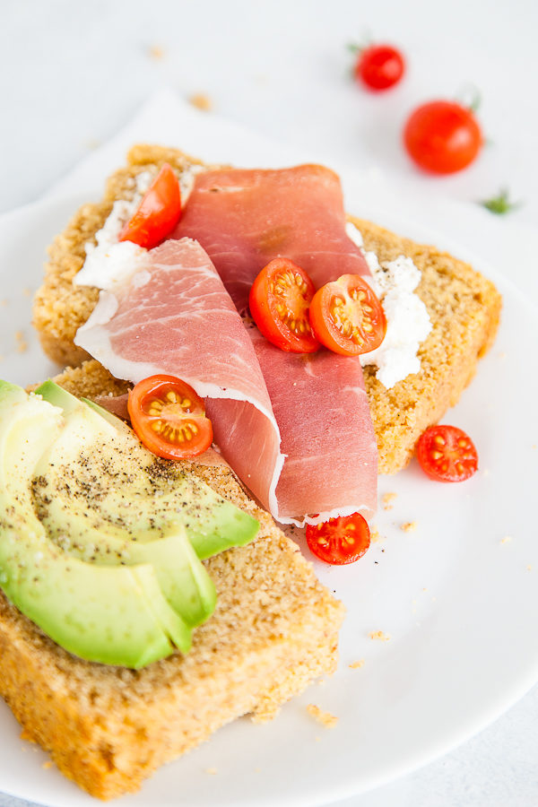 Slices of cornbread with prosciutto, tomatoes, and avocado on top.